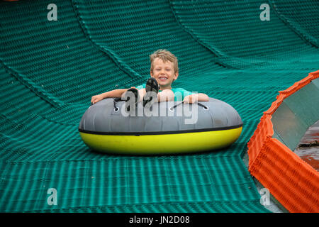 Ragazzo sorridente scorre giù in anello gonfiabile Foto Stock