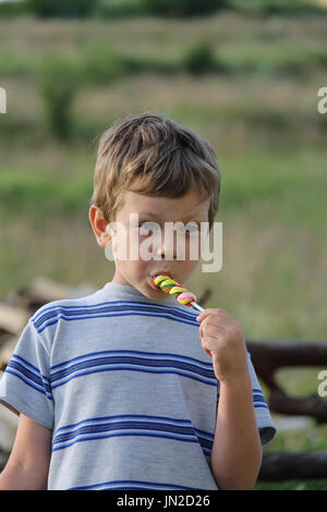 Bel ragazzo mangia caramelle colorate Foto Stock