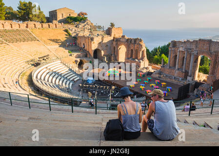 Italia viaggio Sicilia, vista su una serata estiva di una giovane coppia turistica seduto nel teatro greco antico di Taormina, Sicilia. Foto Stock