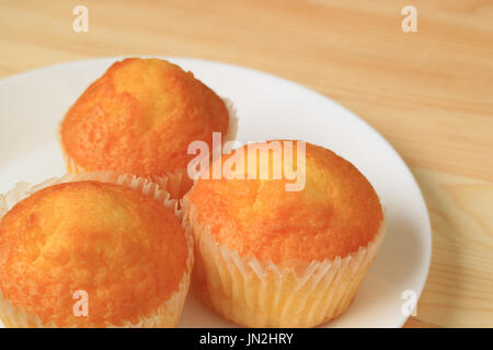 Close-up di tre Madeleine tortine su piastra bianca servita su un tavolo di legno, con sfondo sfocato Foto Stock