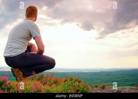 Escursionista in posizione accovacciata su di una roccia in heather boccole, godere del paesaggio Foto Stock