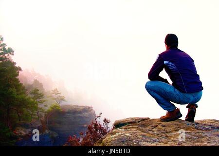 Escursionista in posizione accovacciata su una roccia e godere il paesaggio Foto Stock