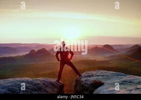 Jumping escursionista in nero celebrano il trionfo tra due picchi rocciosi. Splendida alba. Foto Stock