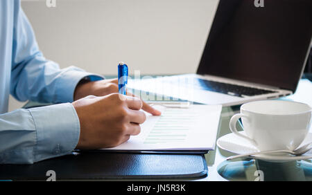 Imprenditore mano che tiene la penna per scrivere il business o i report finanziari sul tavolo con il computer e con una tazza di caffè in affari finanziari o con Foto Stock