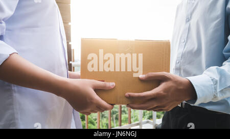 Vicino la mano di asia donna sono di ricevere una scatola da uomo di consegna con luce solare in consegna il concetto di servizio Foto Stock