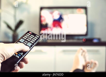 Gli uomini con il telecomando davanti alla TV. Mano con telecomando diretto sulla TV. Un uomo è rilassante e guardare lo sport in TV. Foto Stock