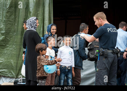 Passau, Germania - 2 Agosto 2015: un poliziotto tedesco sta prendendo cura di un giovane rifugiato bambino dalla Siria all'area di registrazione in Passau, Baviera. T Foto Stock
