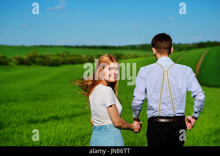 Coppia giovane che corre lungo un campo verde in una bella giornata di sole. Foto Stock