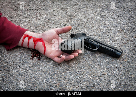 Mano d'uomo sdraiato sul pavimento dopo il suicidio con una pistola Foto Stock