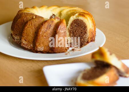 Tradizionale a due colori (marmor) torta madeira sul tavolo di legno, fuoco selettivo sulla torta, servito fette intenzionalmente fuori fuoco. Foto Stock