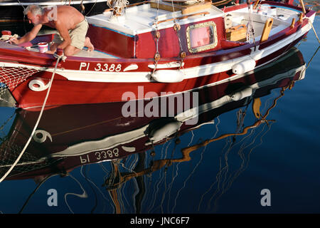 Uomo di verniciatura di un legno classica barca a vela ormeggiata presso la marina di Izola Slovenia con la riflessione nelle limpide acque blu Foto Stock