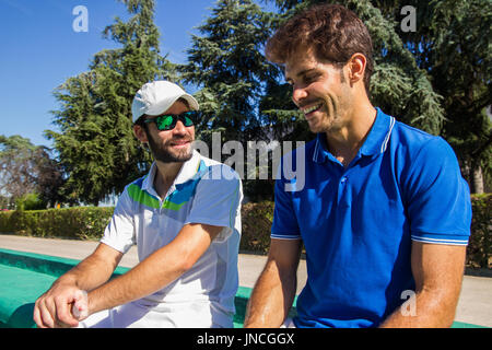 Due giocatori professionisti idratare dopo un duro gioco di tennis. Essi sono gli amici e sono seduti in appoggio per il gioco. Sono felici e ridere. Foto Stock