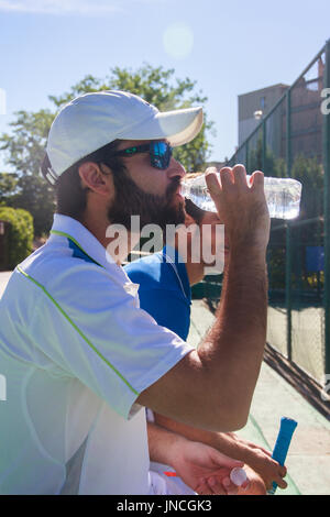 Due giocatori professionisti idratare dopo un duro gioco di tennis. Essi sono gli amici e sono seduti in appoggio per il gioco. Sono felici e ridere. Foto Stock