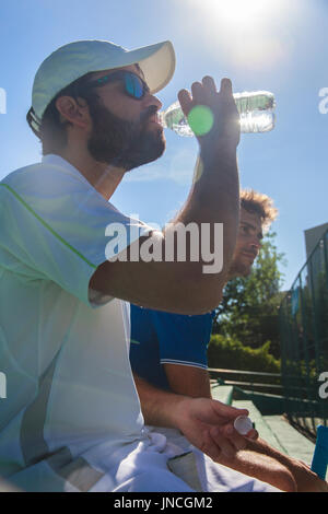 Due giocatori professionisti idratare dopo un duro gioco di tennis. Essi sono gli amici e sono seduti in appoggio per il gioco. Sono felici e ridere. Foto Stock