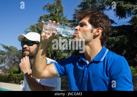 Due giocatori professionisti idratare dopo un duro gioco di tennis. Essi sono gli amici e sono seduti in appoggio per il gioco. Sono felici e ridere. Foto Stock