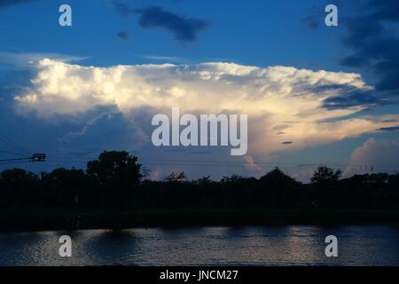 Acque tranquille Parco Lago al tramonto con il bianco delle nuvole sopra la Treeline in distanza Foto Stock