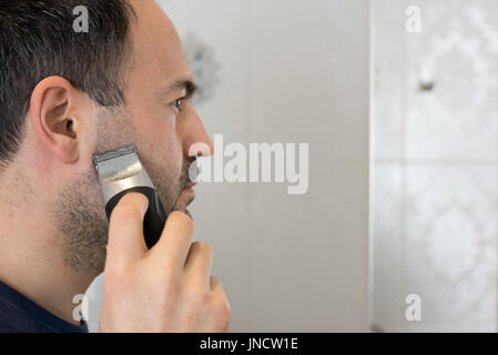 Uomo barba di trimming in bagno con rasoio elettrico sullo specchio Foto Stock