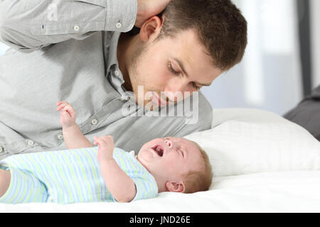 Confuso padre guarda il suo Figlio bambino piange disperatamente su un letto Foto Stock