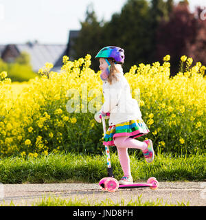 Bambino scooter equitazione sulla via del ritorno a scuola. Bambina giocare all'aperto l'apprendimento in equilibrio su kick board. Kids ride scooter in periferia street. Pres Foto Stock