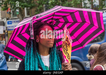Luglio 29, 2017 - Londra, Regno Unito - Londra, Regno Unito. Il 29 luglio 2017. Una donna con una rosa striped ombrello detiene un nero vive questione sulla targhetta all'esterno prrotest Stoke Newington stazione di polizia per Rashan Charles, che morì quando due forze di polizia ammanettato con lui e lo teneva sul pavimento in un negozio sulla Kingsland Rd nelle prime ore di sabato 22 luglio. La sua famiglia sono determinati per ottenere risposte circa la sua morte ma la chiamata per tutti ad agire nel rispetto della legge. Membri della famiglia di Carlo è venuto alla protesta lungo con la famiglia di Edson da Costa, che è morto dopo arresto in East Ham in giugno. Manifestanti hanno tenuto le foto t Foto Stock