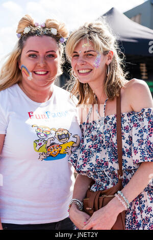 Due giovani donne caucasici, 20s, in posa per il visualizzatore, entrambi sorridenti, contatto visivo. Faccia dipinta con glitter pattern. Bel sorriso su entrambe le donne. Foto Stock