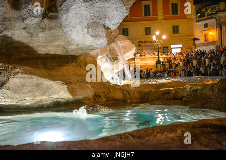 Close up di un flusso di acqua e uno dei pool di Fontana di Trevi a Roma con i turisti in background fino a tarda notte Foto Stock