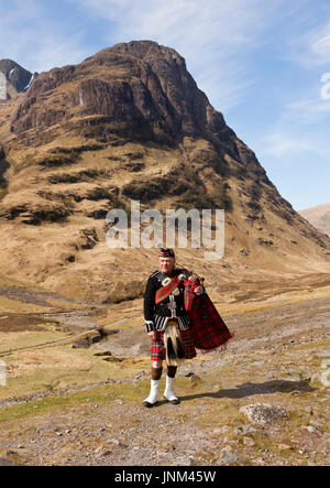 Un piper giocando le cornamuse con un scozzese montagne sullo sfondo Foto Stock