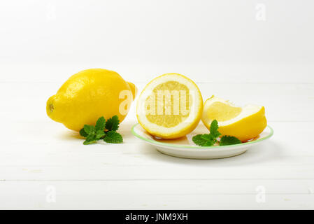 Intero e limoni a fettine su piastra in bianco e lo sfondo in legno Foto Stock