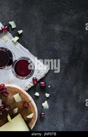 Due bicchieri di vino rosso tritato spagnolo hard formaggio manchego su legno tagliato con uve rosse scuro su sfondo rustico, vista dall'alto con spazio di copia Foto Stock