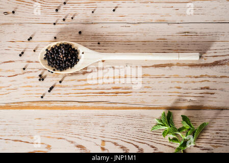 Scatto dall'alto di un cucchiaio di legno su turbati da tavolo, con grani di pepe nero. Foto Stock