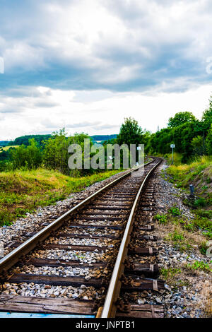 Ferrovie in diagonale tra l'erba verde. Nuvole pesanti su sky, bella immagine colorata. Foto Stock