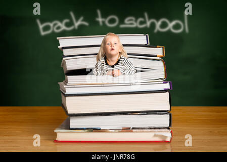 Ragazza bionda indossando spogliato top, spuntano fuori della pila di libri in classe Foto Stock