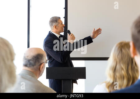 Business altoparlante con microfono dispositivo di puntamento con mano alla lavagna vuota nella parte anteriore del pubblico, conferenza, seminario concept Foto Stock