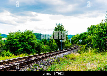 Ferrovie in diagonale tra l'erba verde. Nuvole pesanti su sky, bella immagine colorata. Foto Stock