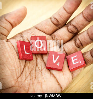 Lettere bianche su legno rossiccio isolati da un gioco di lavoro scrivi la parola 'amore' nel palmo della mano di una persona. La loro palm è aperta rivolta verso la lente. Foto Stock