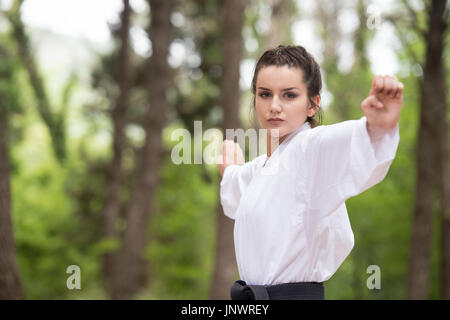 Giovane donna praticanti di Karate di lei si muove nella boscosa Area forestale - Bianco Kimono - Cintura nera Foto Stock