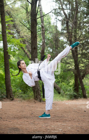 Giovane donna praticanti di Karate di lei si muove nella boscosa Area forestale - Bianco Kimono - Cintura nera Foto Stock