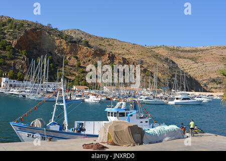 La pesca a strascico ormeggiata in banchina, con persone di pesca dal molo in una calda giornata estiva a Javea sulla Costa Blanca, Spagna. Foto Stock