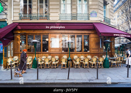 Parigi, Francia - 29 Febbraio 2016: la signora nel cappuccio arancione a piedi il suo cane passato Les Philosophes cafe su Rue Vieille du Temple nel Marais, Parigi. Foto Stock