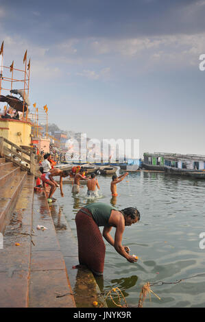 Gli uomini si bagna nel Gange a sunrise e in primo piano un uomo galleggia un sacrificio nel fiume Foto Stock