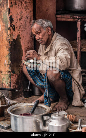 Un chai wallah siede sul suo haunches e aggiunge una moneta per il suo denaro lo stagno Foto Stock
