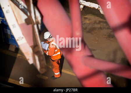 Materiali offshore coordinatore store (l'uomo) leggere il manifesto indossando tute arancione / tute. Credito: lee ramsden / alamy Foto Stock