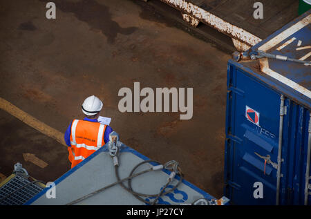 Materiali offshore coordinatore store (l'uomo) leggere il manifesto indossando tute blu / tute. Credito: lee ramsden / alamy Foto Stock