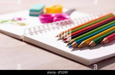 Close up di matite di legno e altre forniture scolastiche sulla nota vuota libro sulla scrivania in legno Foto Stock