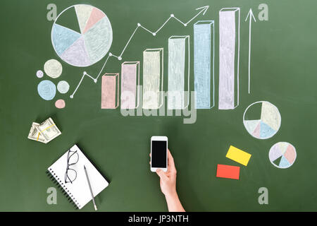Vista superiore della persona business utilizza lo smartphone con schermo vuoto al posto di lavoro, piccolo ufficio concetto Foto Stock