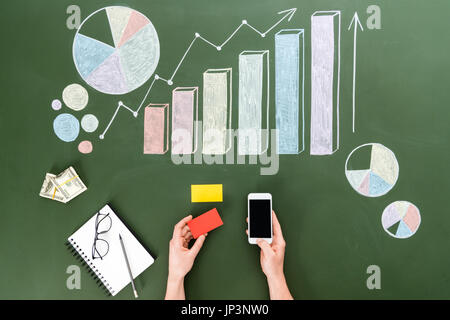 Vista superiore della persona business utilizza lo smartphone con schermo vuoto al posto di lavoro, piccolo ufficio concetto Foto Stock