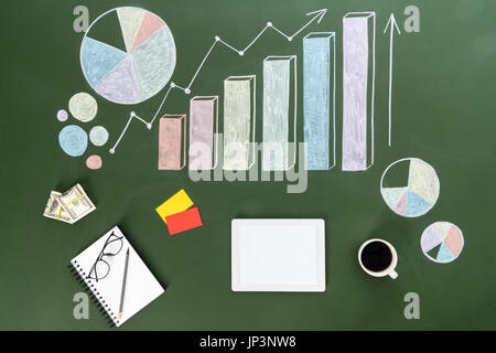 Vista superiore della tavoletta digitale, una tazza di caffè, dollaro banconote e i grafici di business al lavoro, piccolo ufficio concetto Foto Stock