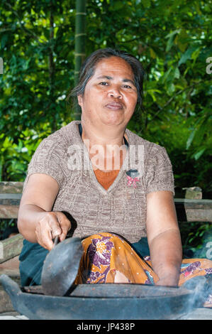 Ubud, Bali, Indonesia - 27 luglio 2013. Contadina seduta sul pavimento, tostatura di cacao in piatti tradizionali Foto Stock