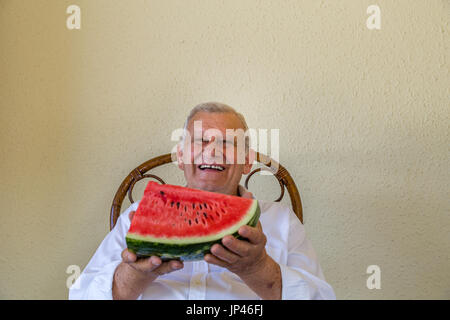 Felice vecchio uomo azienda fetta di cocomero giallo su sfondo a parete Foto Stock