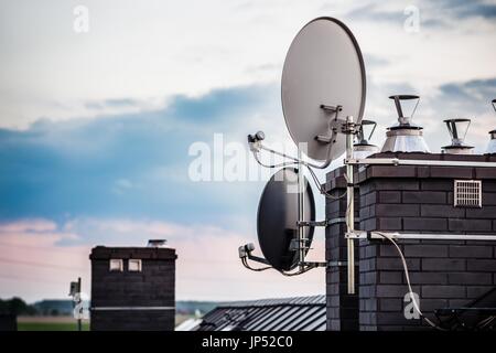 Le antenne paraboliche antenne satellite montato sul camino di una nuova casa. Sera Foto Stock